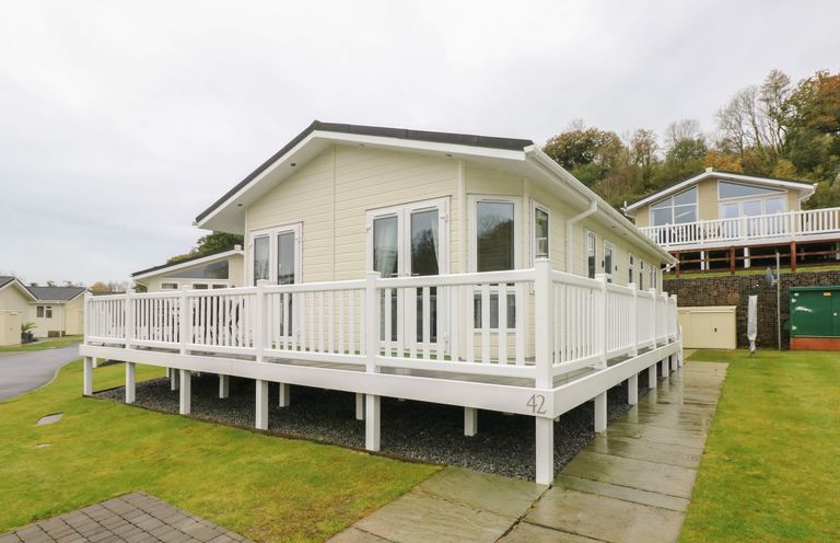 An exterior view of a beige lodge with white railings on a raised deck at Cwtch Lodge 42 Stepaside near Wisemans Bridge