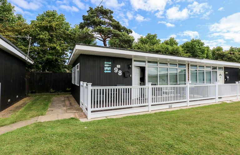 A black house with white railing and a grassy front yard at 98 Cherry Park in Chapel St Leonards