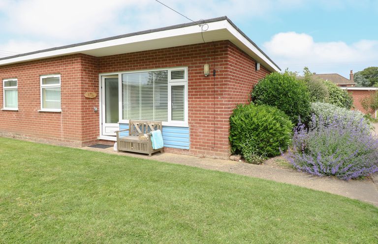 A brick house with a bench and plants outside on a lawn at The Nook in Mundesley