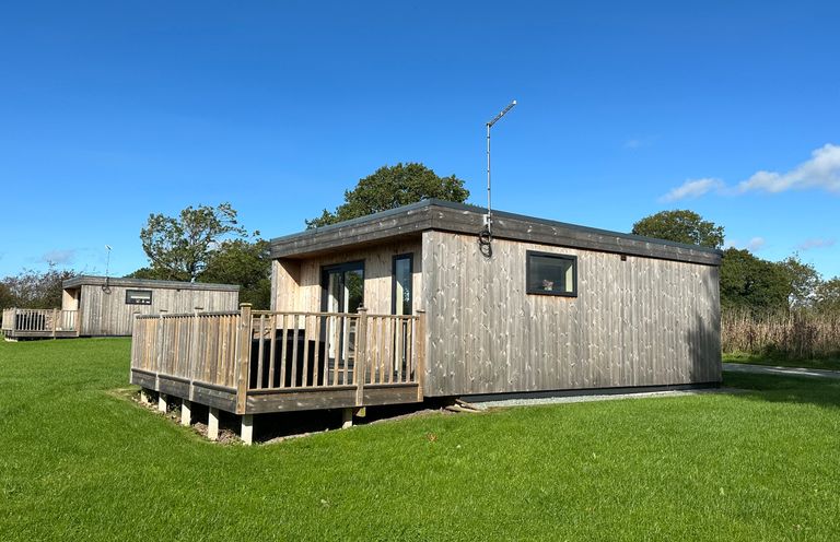 A wooden cabin with a deck and railing on a grassy area with another cabin in the background at The Wren in Wem