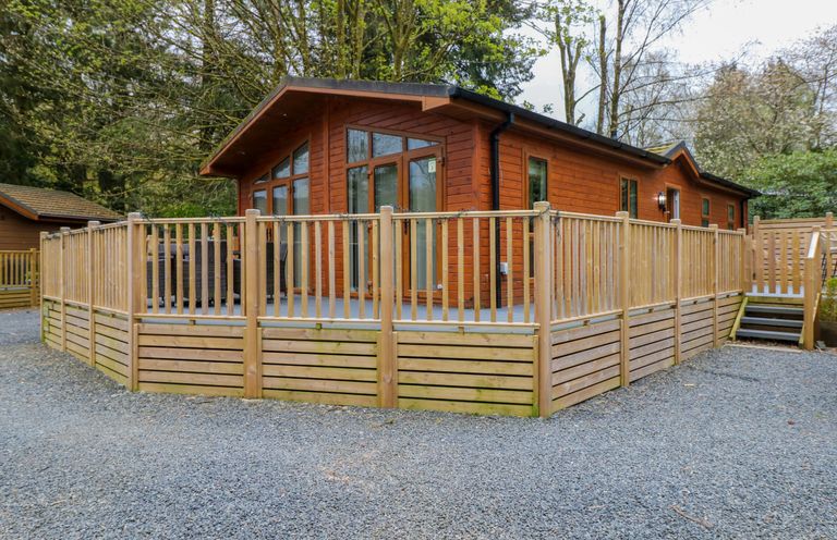 A wooden cabin with a large deck and railing surrounded by trees at Oakwood Lodge Langdale 3 White Cross Bay Windermere