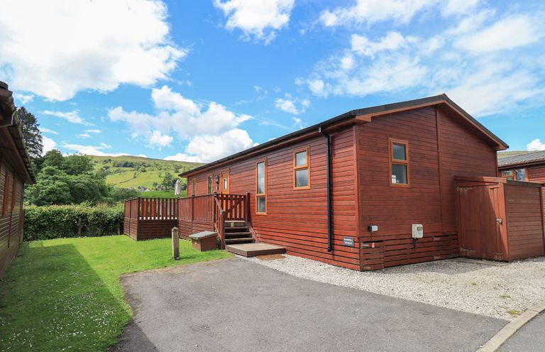 A wooden cabin with a small deck and steps leading to the entrance surrounded by grass and a paved driveway at Wansfell Retreat Lodge Wansfell 4 Limefitt Park near Windermere