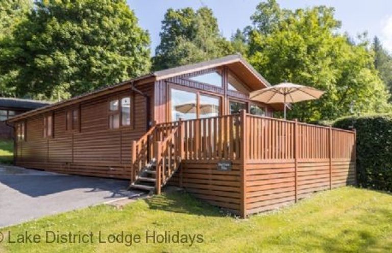 A wooden lodge with a deck and umbrella surrounded by trees at Sheffield Pike Lodge Ullswater 8 Limefitt Park near Windermere