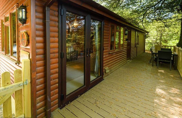 A wooden cabin exterior with glass double doors and outdoor dining table on a deck surrounded by trees at Lakeshaven Skiptory Howe 16 White Cross Bay near Windermere