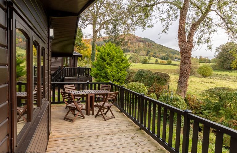 A wooden deck with a table and chairs overlooking a grassy field and hills at Glaramara Number 7 Burnside Park near Keswick