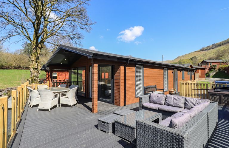 An outdoor deck area with wicker seating and dining table attached to a wooden lodge in a rural setting Jinnyspinner Lodge in Beckside 37 Limefitt Park near Windermere
