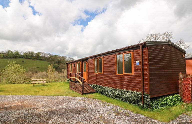 A wooden mobile home with windows and a small ramp outside surrounded by grass and hills at Exe Valley Lodge in Bampton Devon