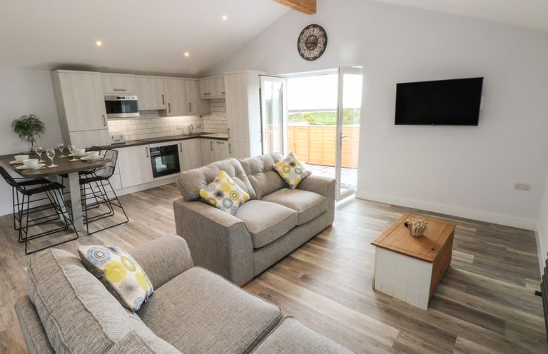 An open plan living room and kitchen with sofas a dining table and a wall mounted TV at Caban Y Mor in Amroth near Saundersfoot