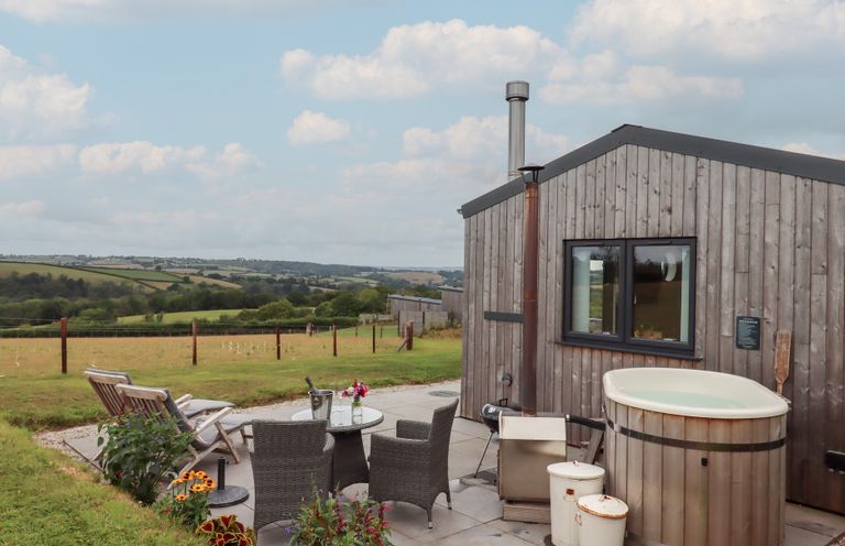 An outdoor area with a wooden cabin, hot tub, table and chairs at The Pennymoor Cadeleigh near Tiverton