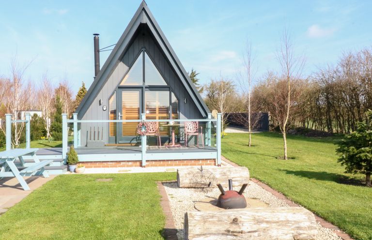 A gray A-frame cabin with a deck and outdoor seating in a grassy yard at Silver Birch Lodge in Misterton