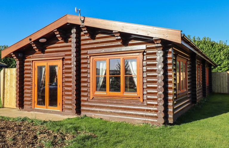 A log cabin with wooden framed windows and doors surrounded by grass at Elm Lodge Greetham Rutland