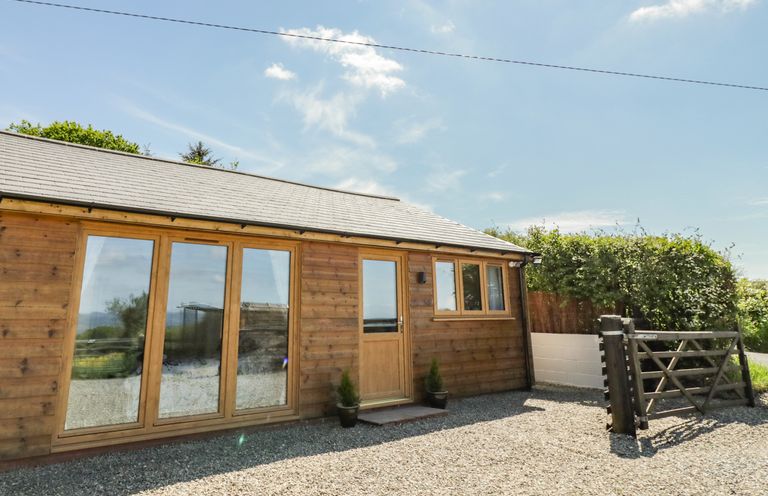 A wooden building with large glass doors and a small window beside a gravel driveway with a wooden gate at FAIRFIELD in Clee Hill