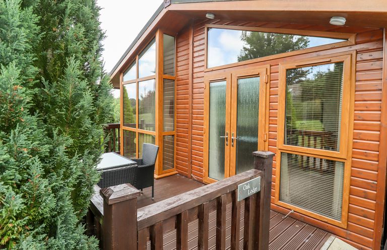 A wooden lodge exterior with glass doors and windows and outdoor seating at Oak Lodge in Glasshouse