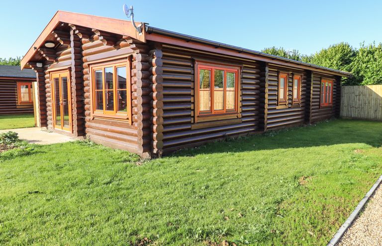 A wooden log cabin with multiple windows and a glass door on a grassy lawn at Holly Lodge in Greetham Rutland
