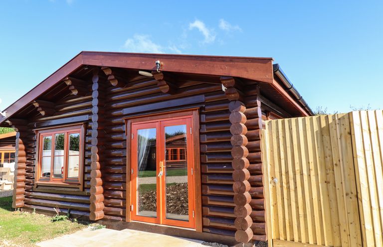 A wooden log cabin with double glass doors and a window next to a wooden fence at Pine Lodge in Greetham Rutland