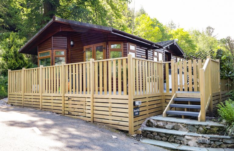 A wooden lodge with a fenced deck and steps surrounded by trees at Broad Oak Lodge in Applethwaite 7 Limefitt Park near Windermere