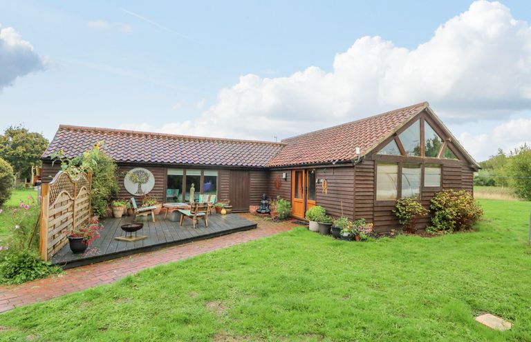 A single-story wooden house with a tiled roof a wooden deck with outdoor furniture and plants on a lawn at The Lodge in Hickling near Catfield