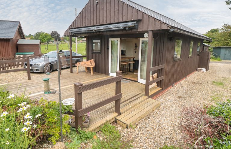 Exterior view of a wooden lodge with a deck and garden area with flowers and a parked car at 3 Valley View Lodges Nawton near Helmsley