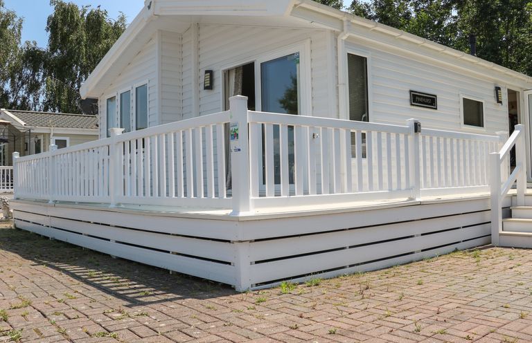 An exterior view of a white mobile home with a wraparound deck and railing at The Goodwood Lodge in Runcton near Chichester