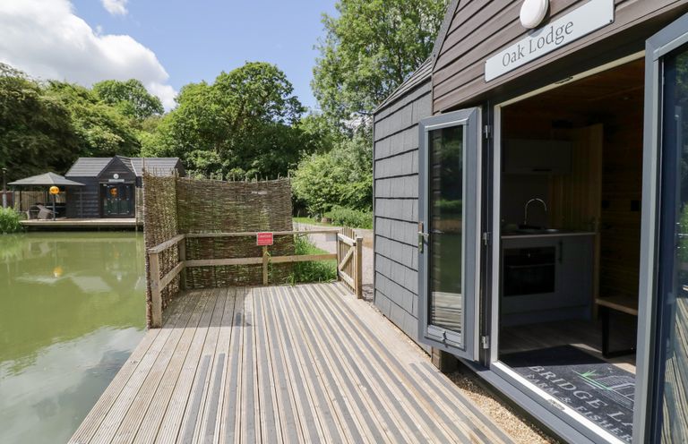 An outdoor view of a lodge by the water at Oak Lodge At Bridge Lake Farm & Fishery Chacombe