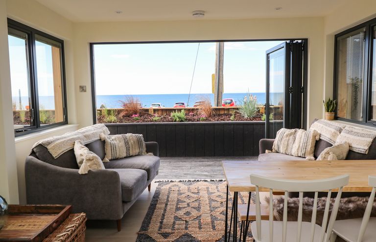 A sitting area with two sofas and a dining table with chairs overlooking the sea at Sandpiper Chalet in Eype