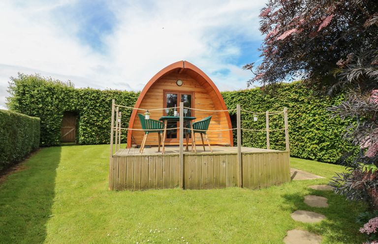 A wooden pod with a deck and table with chairs in a garden surrounded by hedges at Lovesome Pod in Lovesome Hill near Northallerton