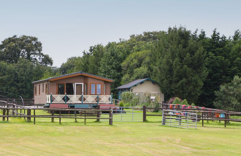 A wooden cabin with a fenced yard and a smaller shed behind surrounded by trees at Hill View Lilac Lodge in Wareham