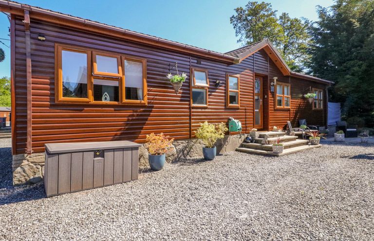 The exterior of a wooden cabin with several windows a door steps with potted plants gravel ground and outdoor seating at RoseGrace Lodge in Auchterarder