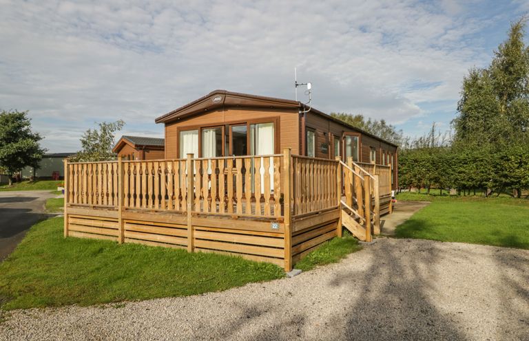 A wooden mobile home with a fenced deck and a gravel driveway at 22 Sherwood South Lakeland Leisure Village near Warton