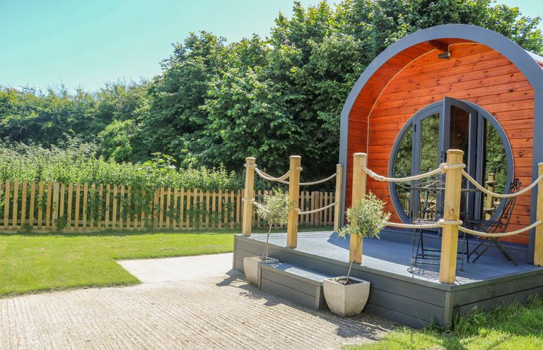 A circular wooden pod with a small porch and potted plants surrounded by a fenced garden at Filbert Pod in Arundel West Sussex