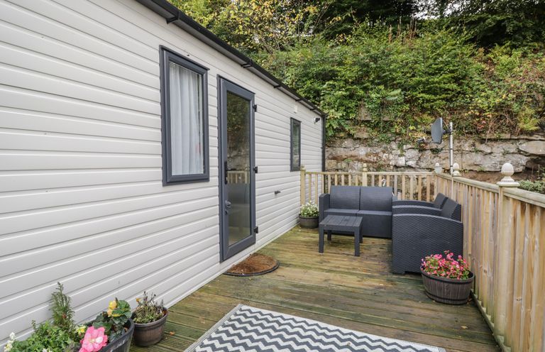 An outdoor deck with black patio furniture and potted plants next to a white building at Burlees Nest in Brigham near Great Broughton Cockermouth