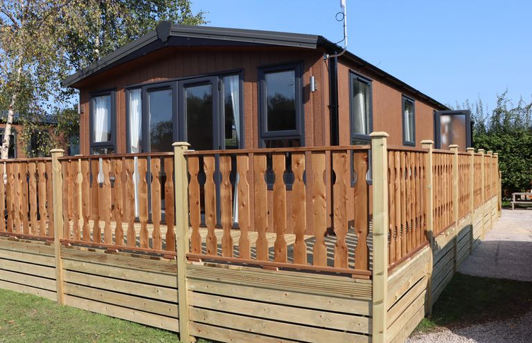 A brown lodge with multiple windows and a wooden railing around the deck at Hawthorn Lodge in South Lakeland Leisure Village
