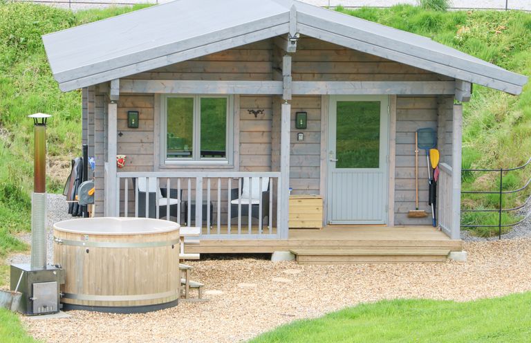 A small wooden cabin with a porch and hot tub outside at Otters Holt in Winston near Staindrop