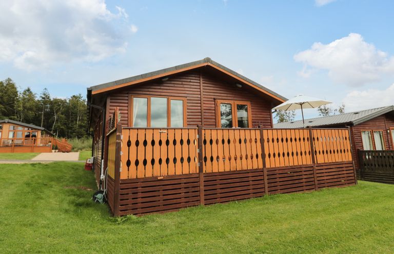 A wooden cabin with a fenced deck and umbrella on grass at Hillside View in Alnwick