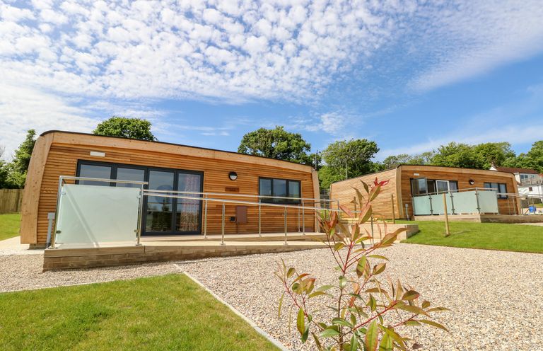 Two wooden modern cabins with glass railings on a gravel and grass lawn under a partly cloudy sky at Barolo in Seaview