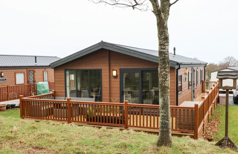 A wooden lodge with large sliding glass doors and a fenced wooden deck in a grassy area at Woodpecker Lodge in Dunbar