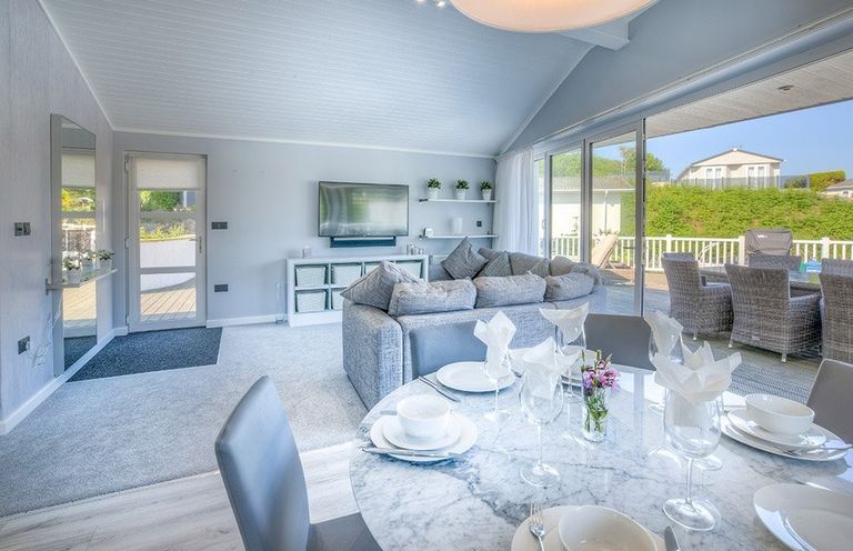 A dining table set with plates glasses and napkins next to a living room with a sofa and a wall-mounted television at The Warren Q4 in Abersoch