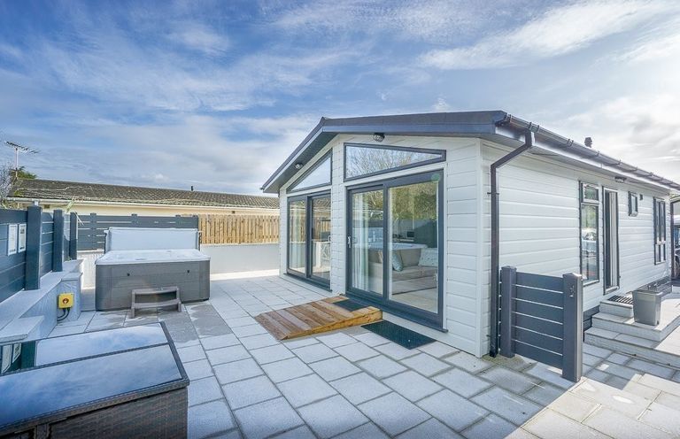 An outdoor patio area with a hot tub sliding glass doors and a small gate at The Warren T23 in Abersoch