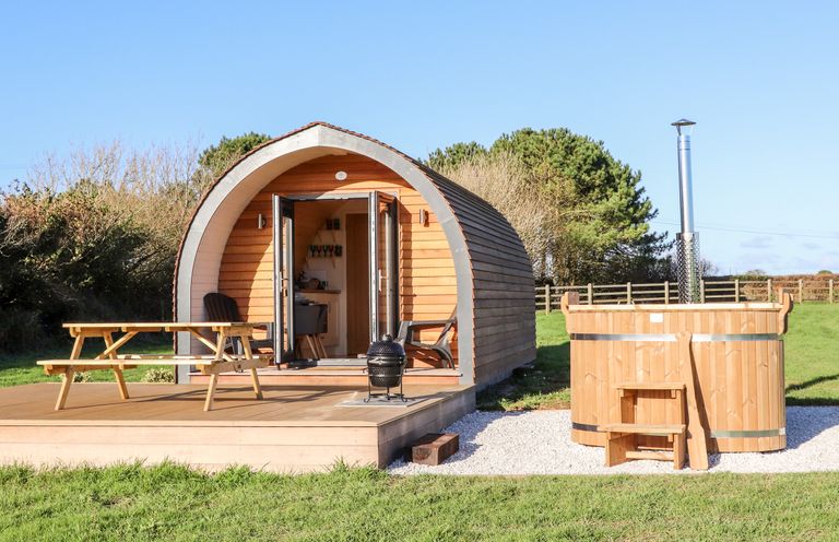 A wooden pod cabin with open doors on a deck with a picnic table and a wooden hot tub nearby at Sea View in St Buryan