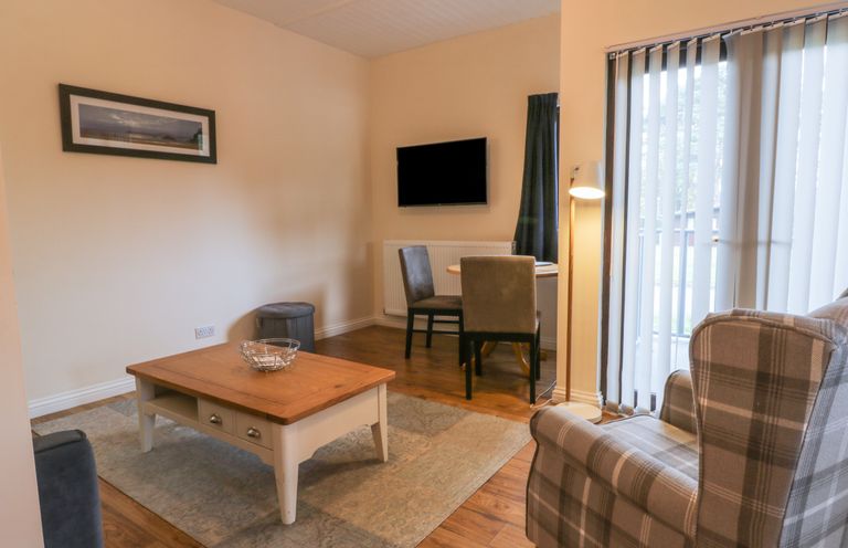 A living room with a wooden coffee table a wall-mounted television a small dining table with two chairs and a plaid armchair at Bugle in Saltburn-By-The-Sea