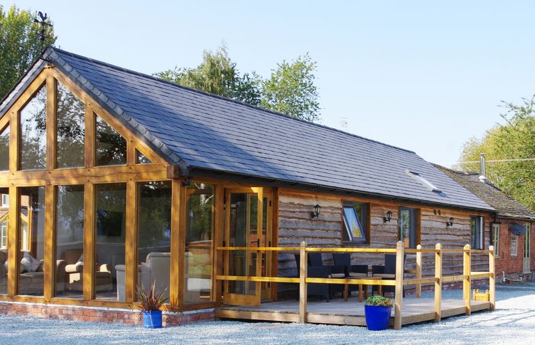 A wooden cabin with large glass windows and a small porch with chairs and tables at Haimwood Byetake in Llandrinio