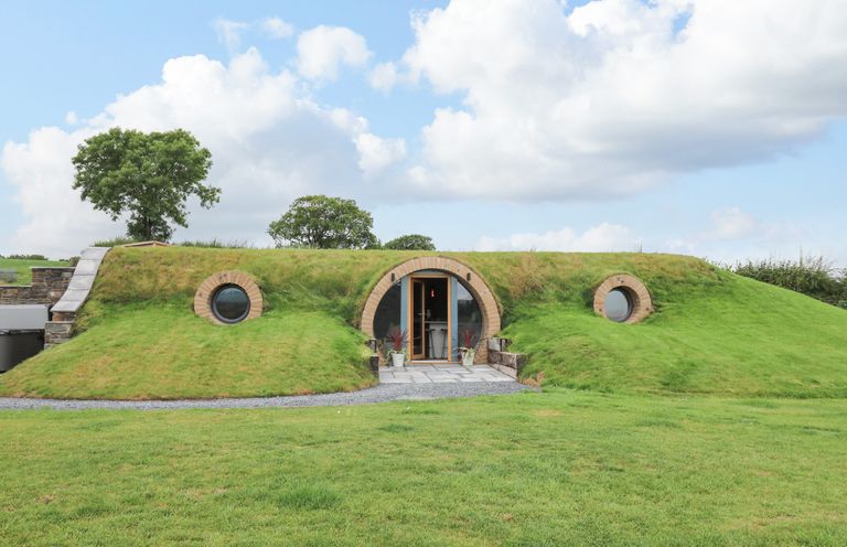 A grass covered earth house with circular windows and an arched doorway surrounded by a lawn at Tan Y Wawr - Derwen in Llanfair Caereinion