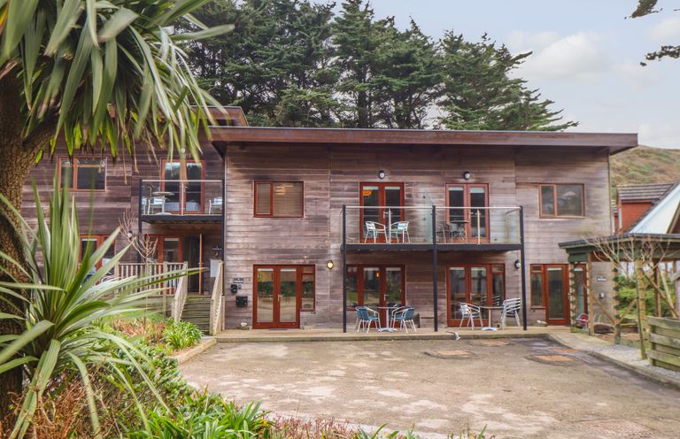 A wooden building with balconies and patio furniture surrounded by trees at Tolcarne in Porthtowan