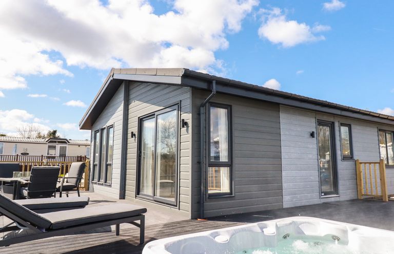 A patio with lounge chairs a hot tub and a modern lodge building at Acorn Lodge in St Day