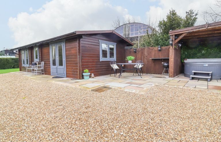 A wooden cabin with outdoor seating and a covered hot tub on a stone patio at Westfield Lodge in Terrington near Sheriff Hutton