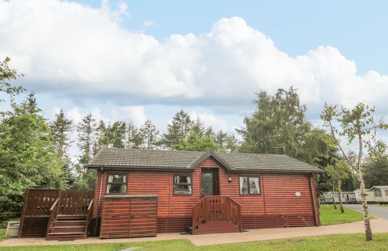 A wooden cabin with a small porch and stairs surrounded by grass and trees at 4 The Oaks in Swarland