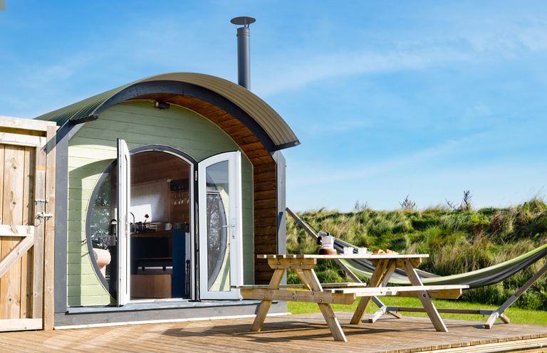 A wooden cabin with curved roof and open doors next to a picnic table and hammock on a wooden deck at Dew Pond in Blagdon