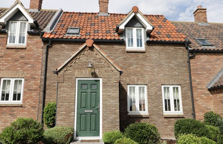 Front view of a brick house with green door and white framed windows with bushes in front at Meadow View in Filey