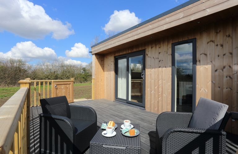 An outdoor wooden deck with black wicker chairs and a table with coffee cups and cakes at The Swift in Wem