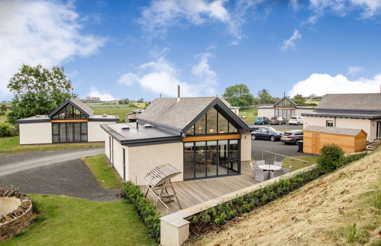 A view of modern houses with a wooden deck and outdoor seating in a rural area at Forget Me Not Lodge Bamburgh